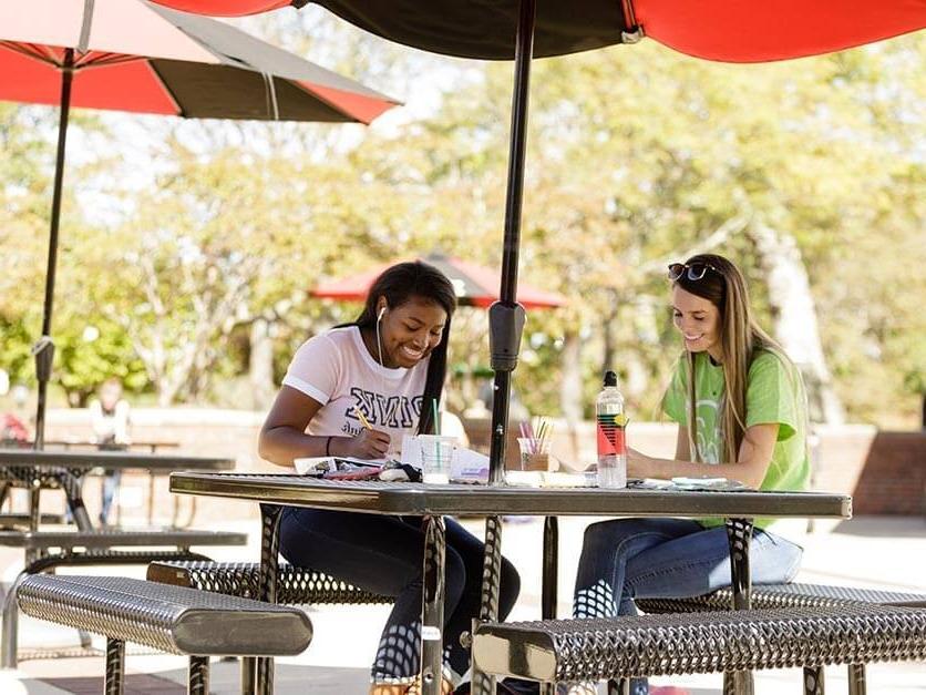 Students laughing and studying under an umbrella in Shaw Plaza